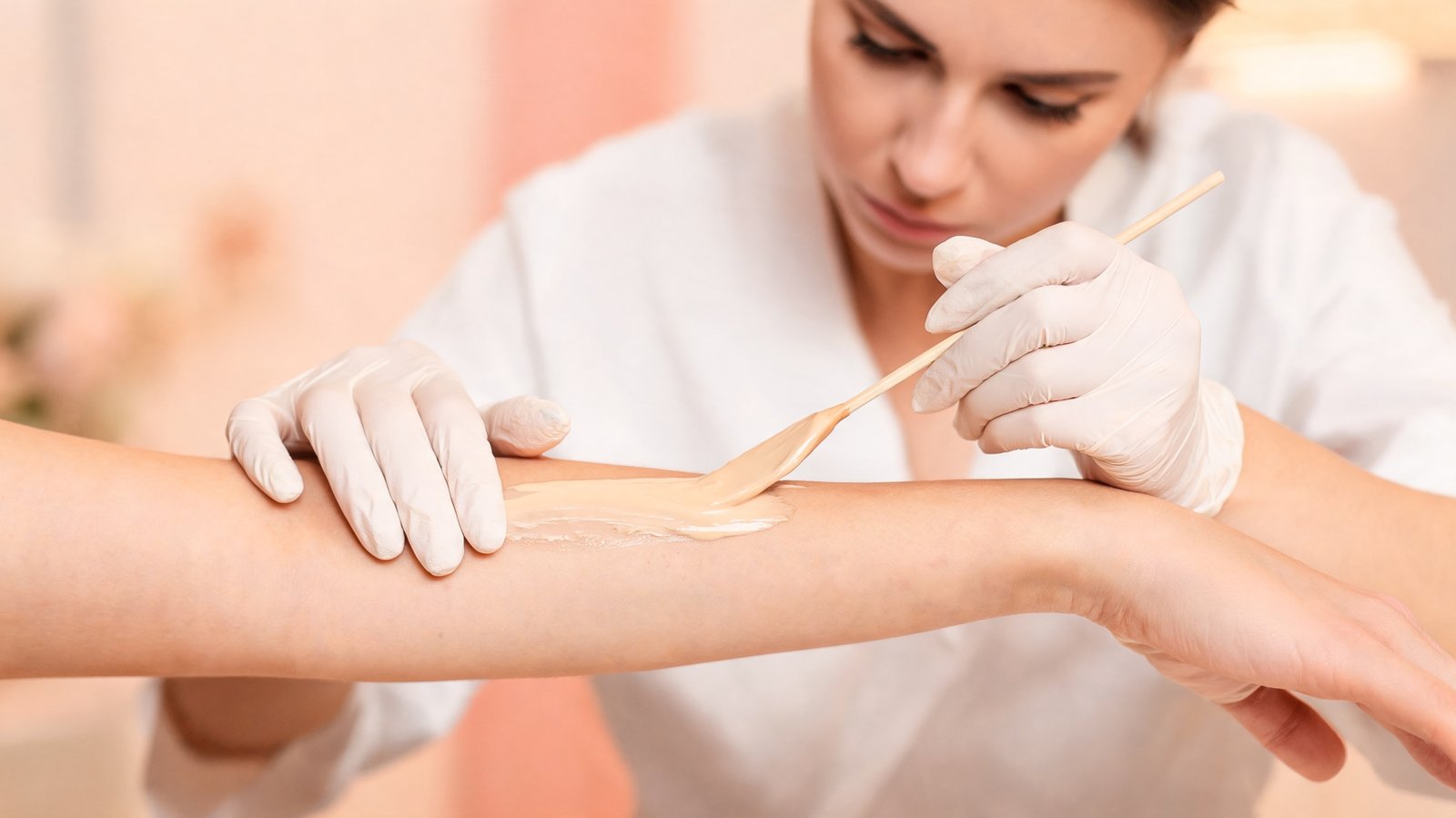 Esthetician applying wax to client's forearm in a clean professional studio